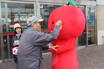 おじいさんがみまもりんごに赤い羽根をつけてもらっている様子